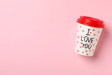 Paper cup with phrase I Love You on pink background, top view