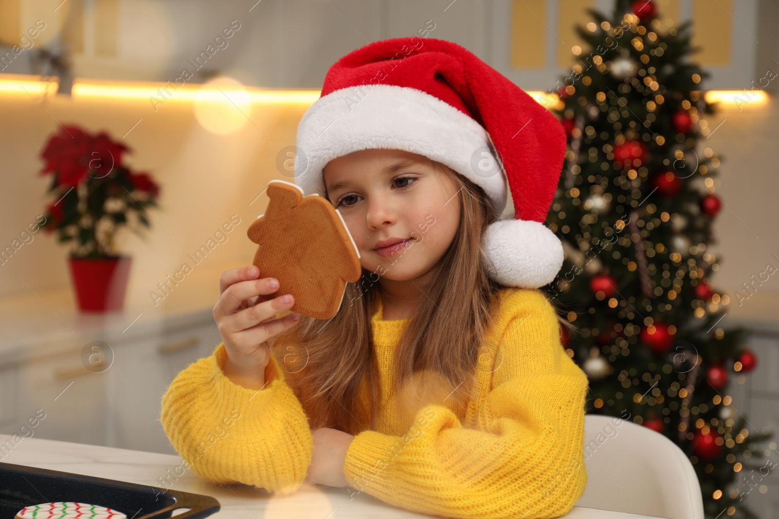 Photo of Cute little girl with Christmas gingerbread cookie at table indoors