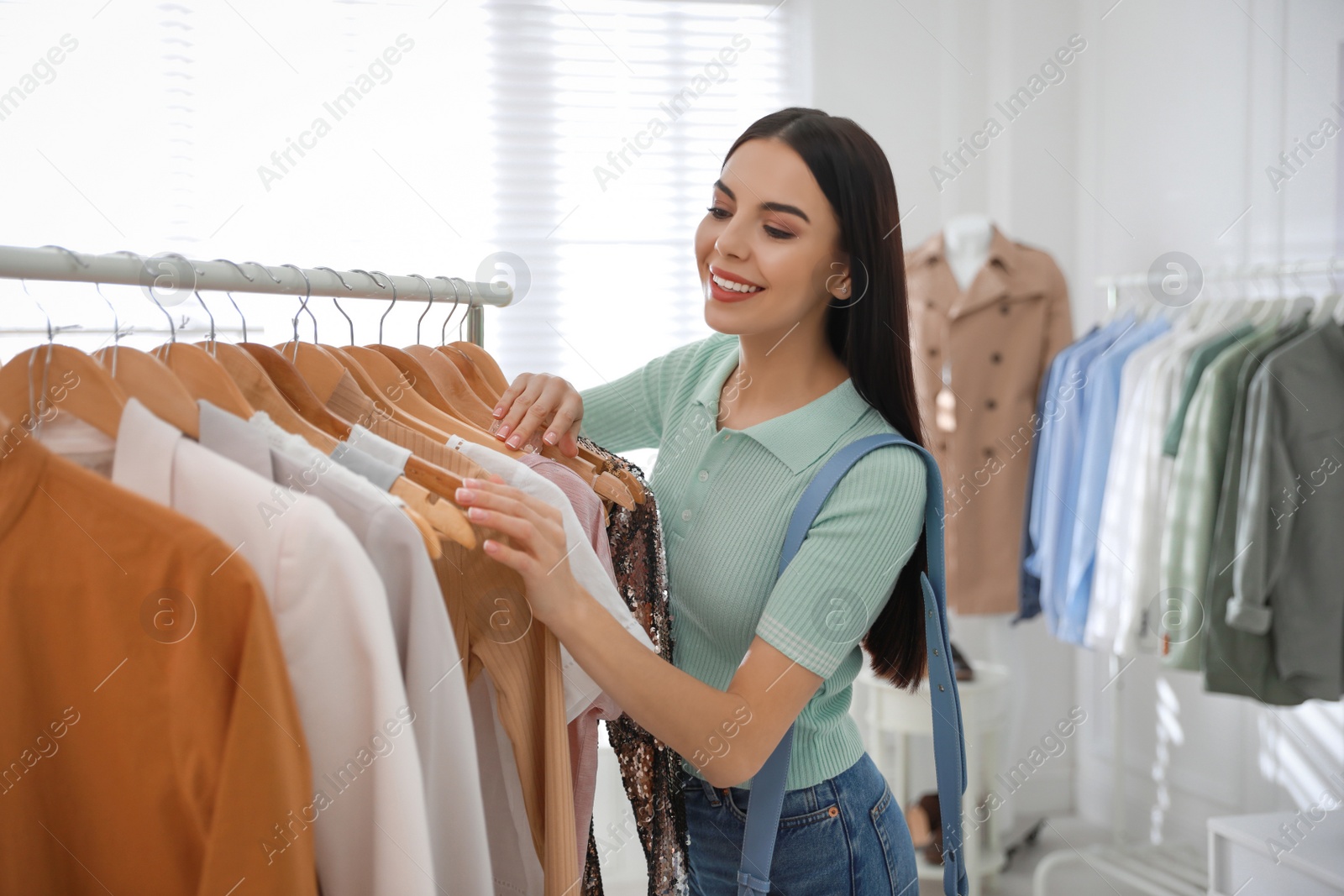 Photo of Young woman choosing clothes near rack in modern boutique