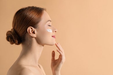 Beautiful young woman with sun protection cream on her face against beige background, space for text