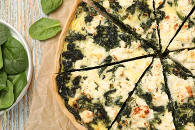 Delicious homemade quiche and fresh spinach leaves on table, flat lay