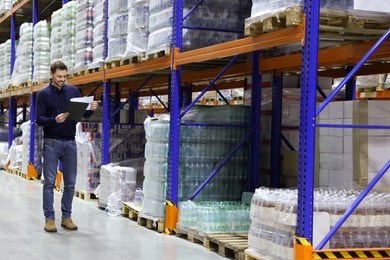 Happy manager holding clipboard in warehouse with lots of products