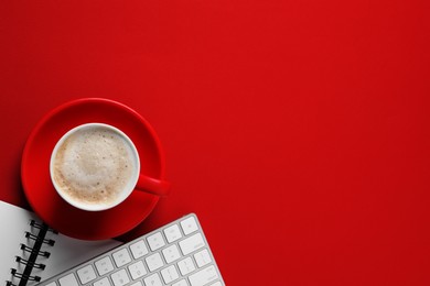 Cup with aromatic cappuccino, notepad and keyboard on red background, flat lay. Space for text