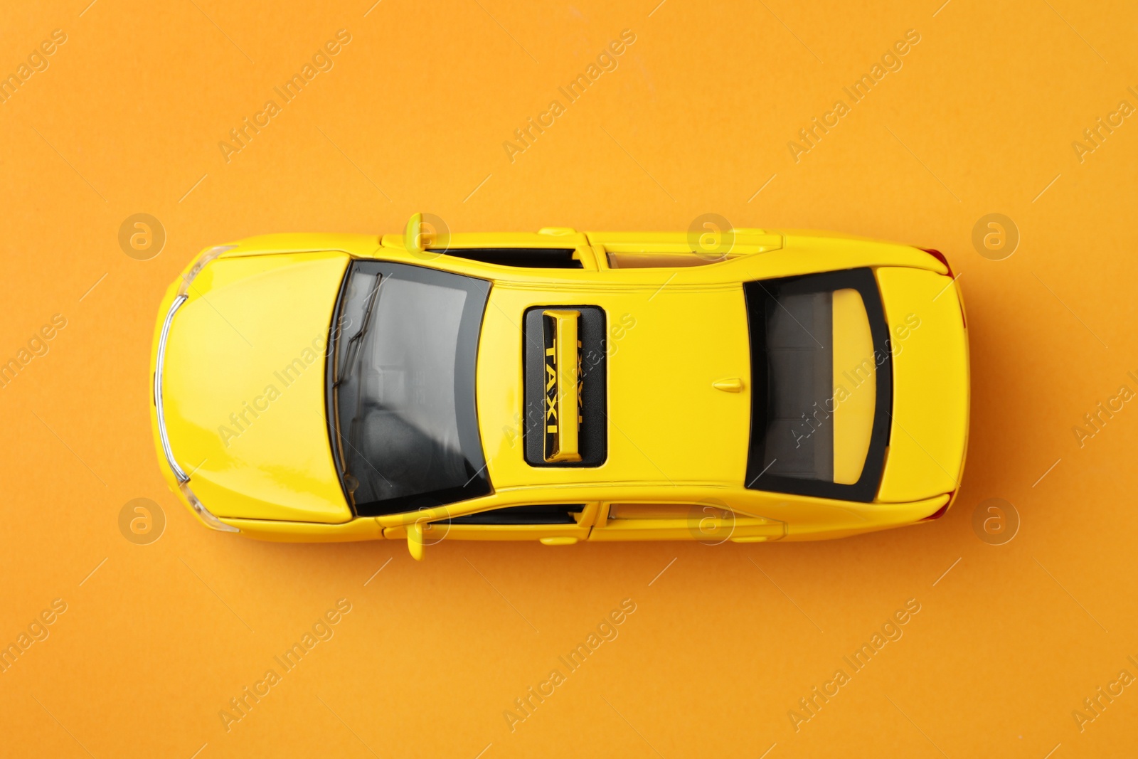 Photo of Yellow taxi car model on orange background, top view