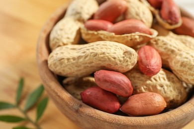 Fresh unpeeled peanuts in bowl on table, closeup