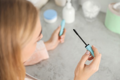 Photo of Young woman holding mascara brush with fallen eyelashes indoors