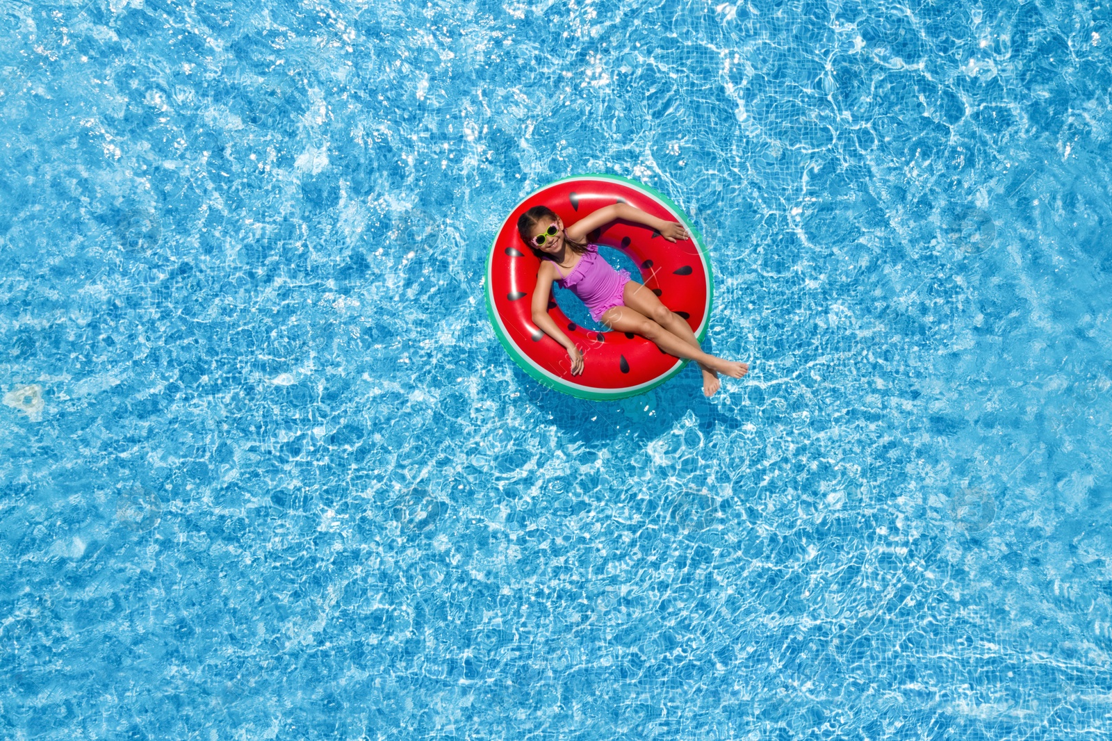 Image of Cute little girl with inflatable ring in swimming pool, top view