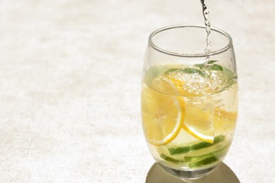 Photo of Pouring water into glass with lemon slices and mint at light grey table, closeup. Space for text