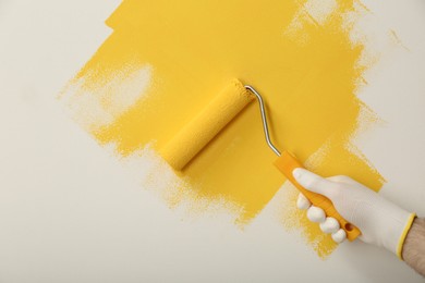 Man applying yellow paint with roller brush on white wall, closeup