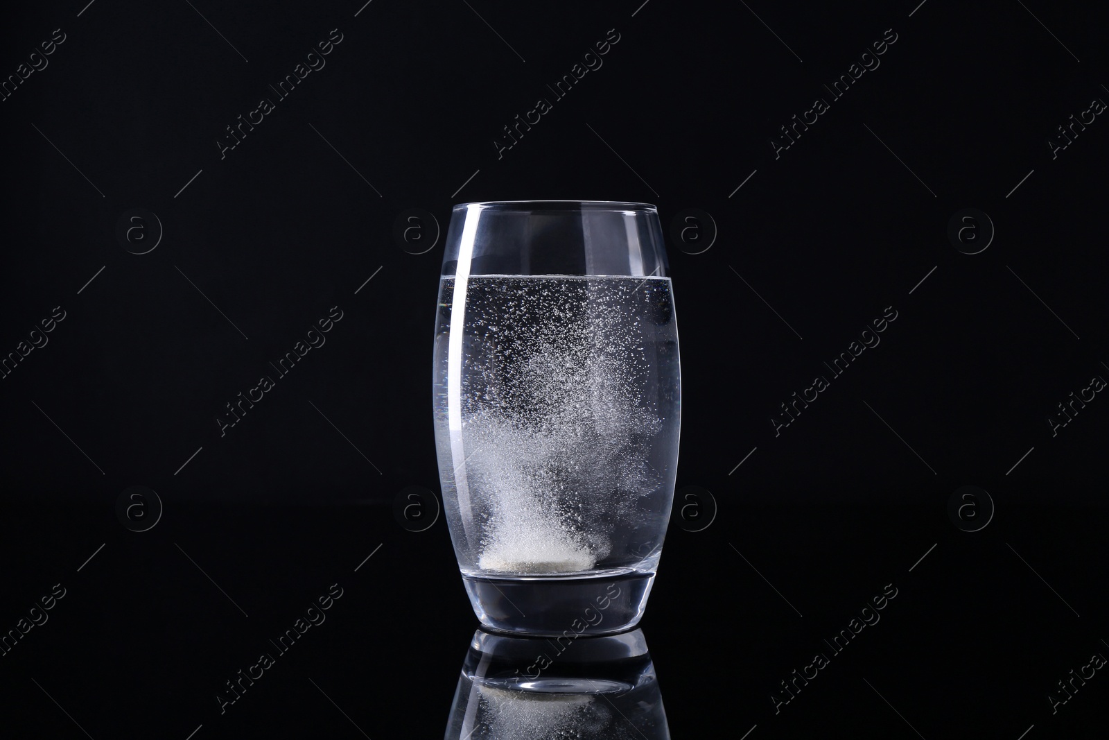 Photo of Effervescent pill dissolving in glass of water on black background