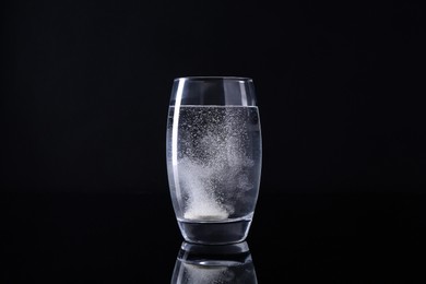 Effervescent pill dissolving in glass of water on black background