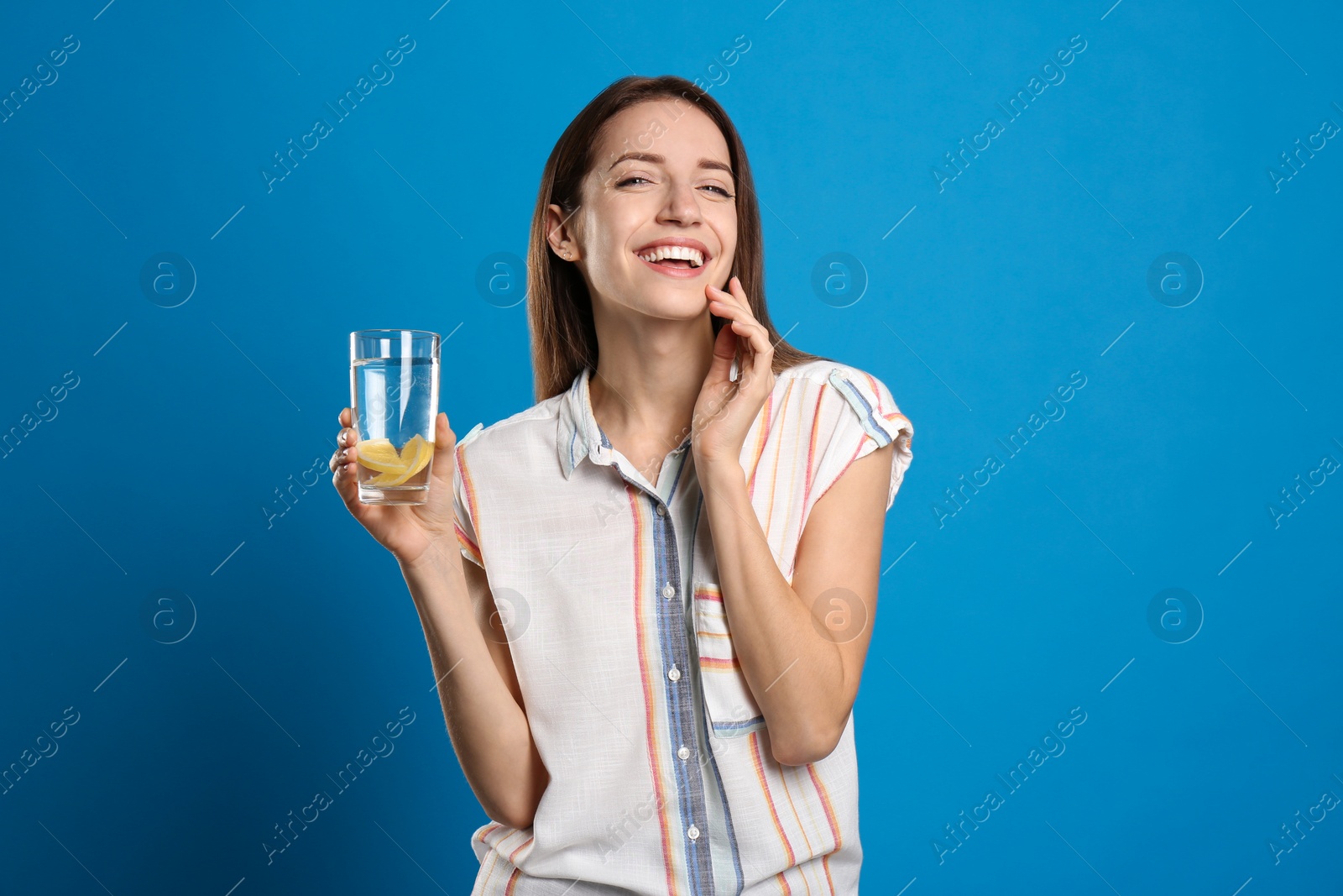 Photo of Young woman with glass of lemon water on light blue background