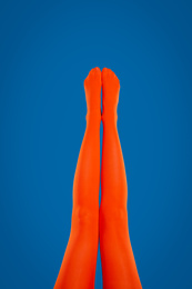 Woman wearing orange tights on blue background, closeup of legs