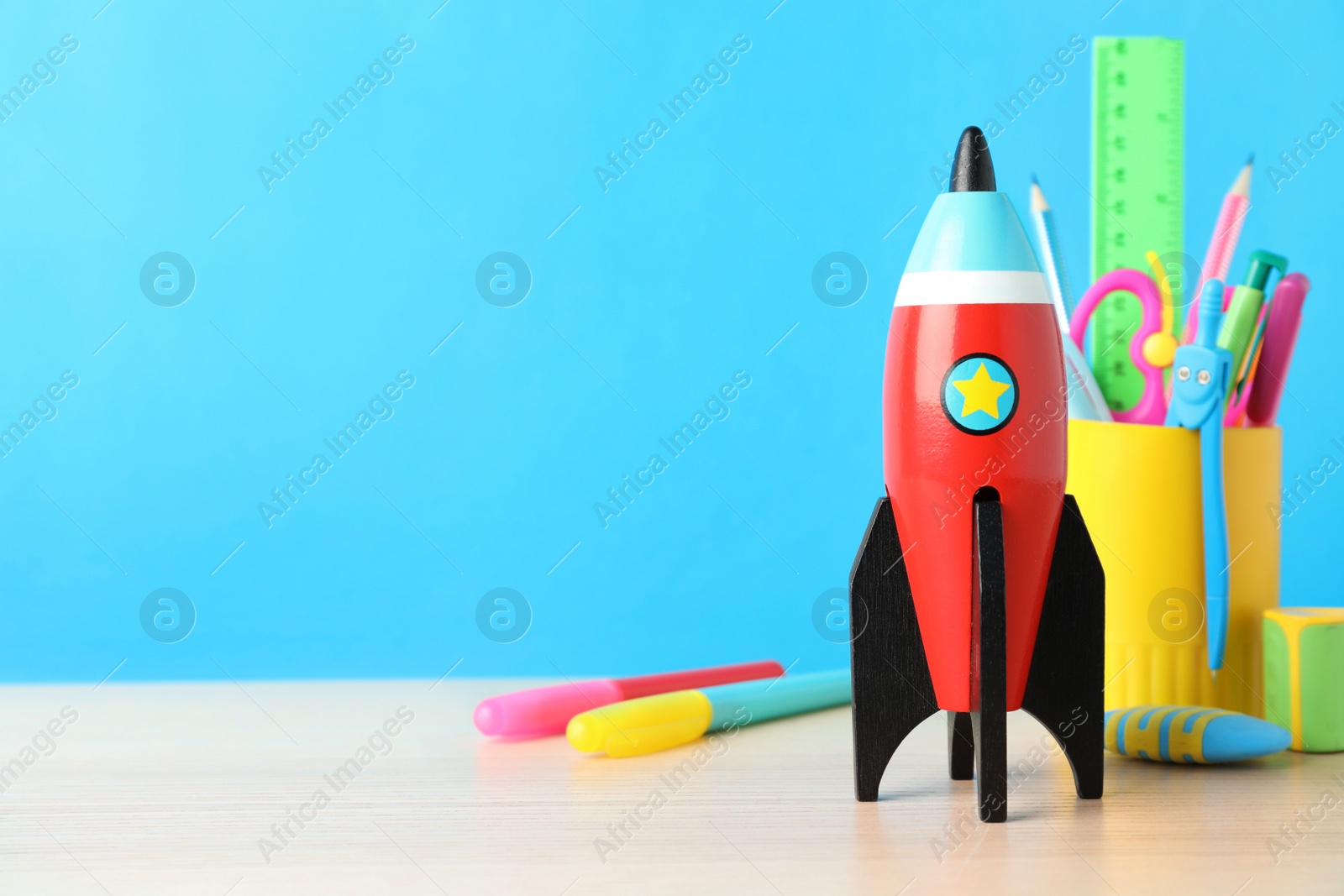 Photo of School stationery and rocket on wooden table against light blue background. Space for text