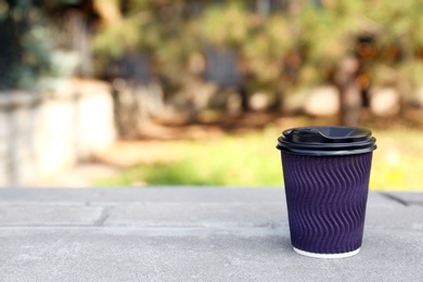 Photo of Cardboard coffee cup on stone parapet outdoors. Space for text
