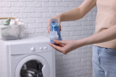 Woman pouring fabric softener from bottle into cap for washing clothes indoors, closeup