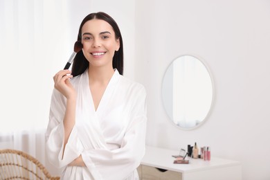 Photo of Beautiful young woman applying makeup with brush at home. Space for text
