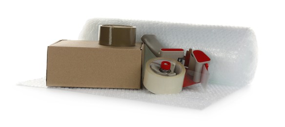 Photo of Bubble wrap roll, cardboard box and tape dispenser on white background