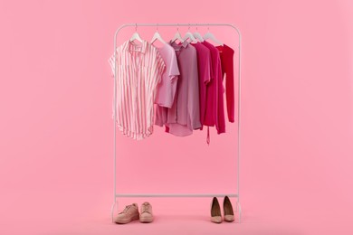 Rack with different stylish women's clothes and shoes on pink background