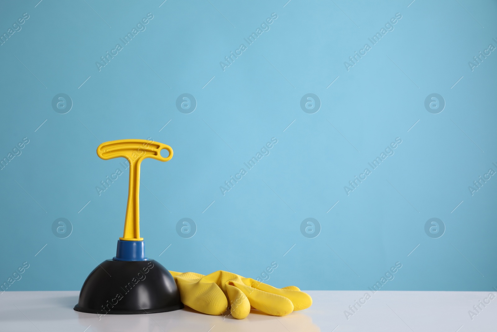 Photo of Plunger and rubber glove on white table against turquoise background. Space for text