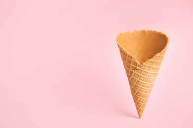 Photo of Empty wafer ice cream cone on pink background. Space for text