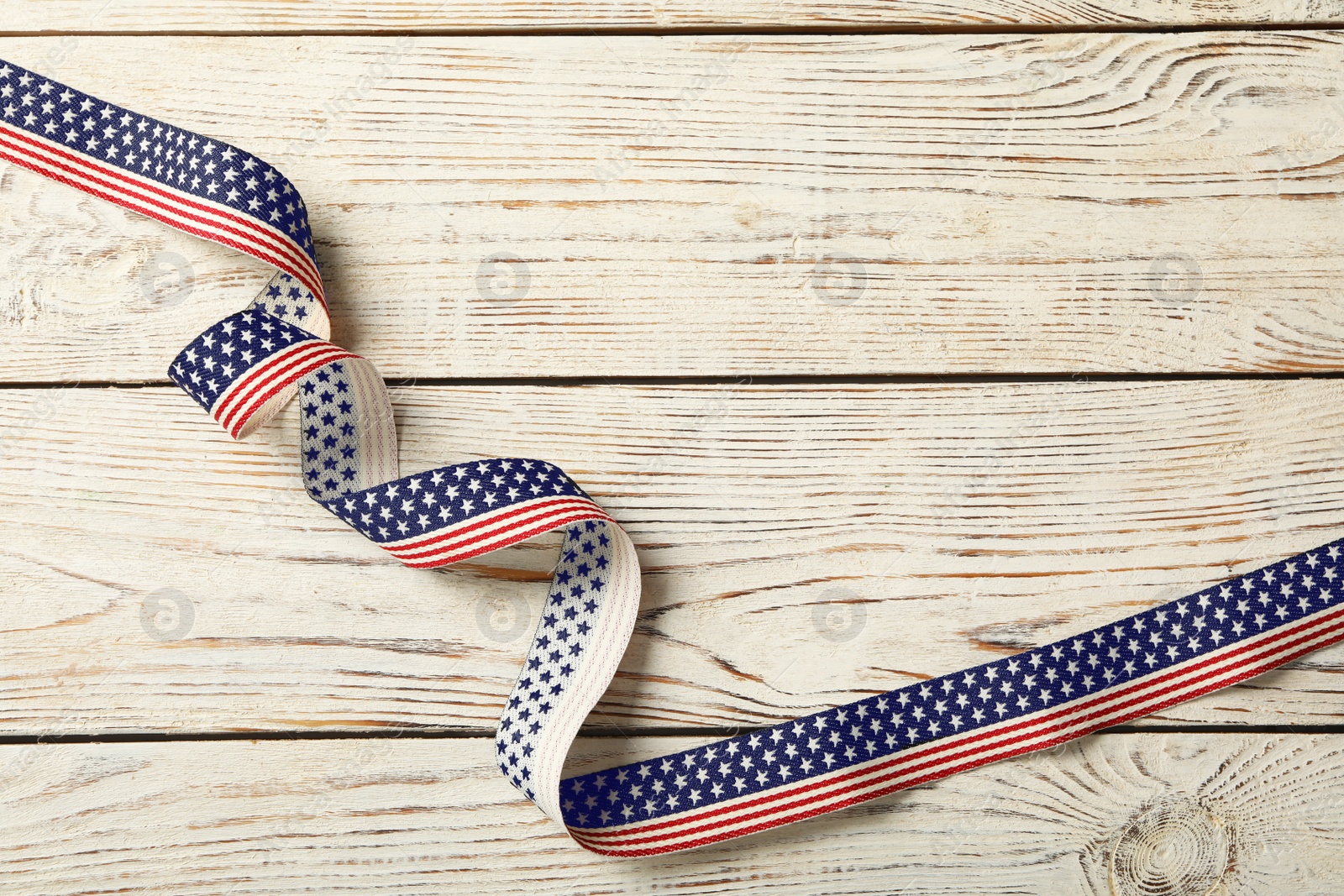 Photo of Ribbon with American flag pattern on white wooden table, top view and space for text. Memorial Day