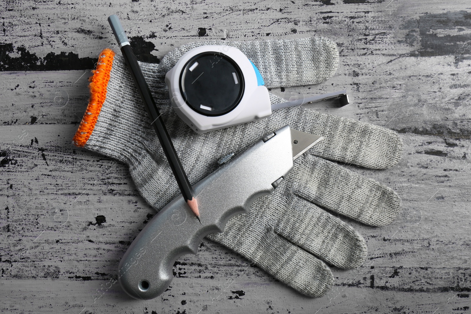 Photo of Utility knife,measuring tape, pencil and glove on rustic table, top view