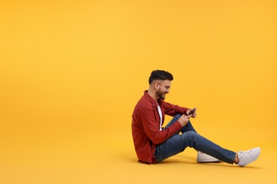 Happy young man using smartphone on yellow background, space for text