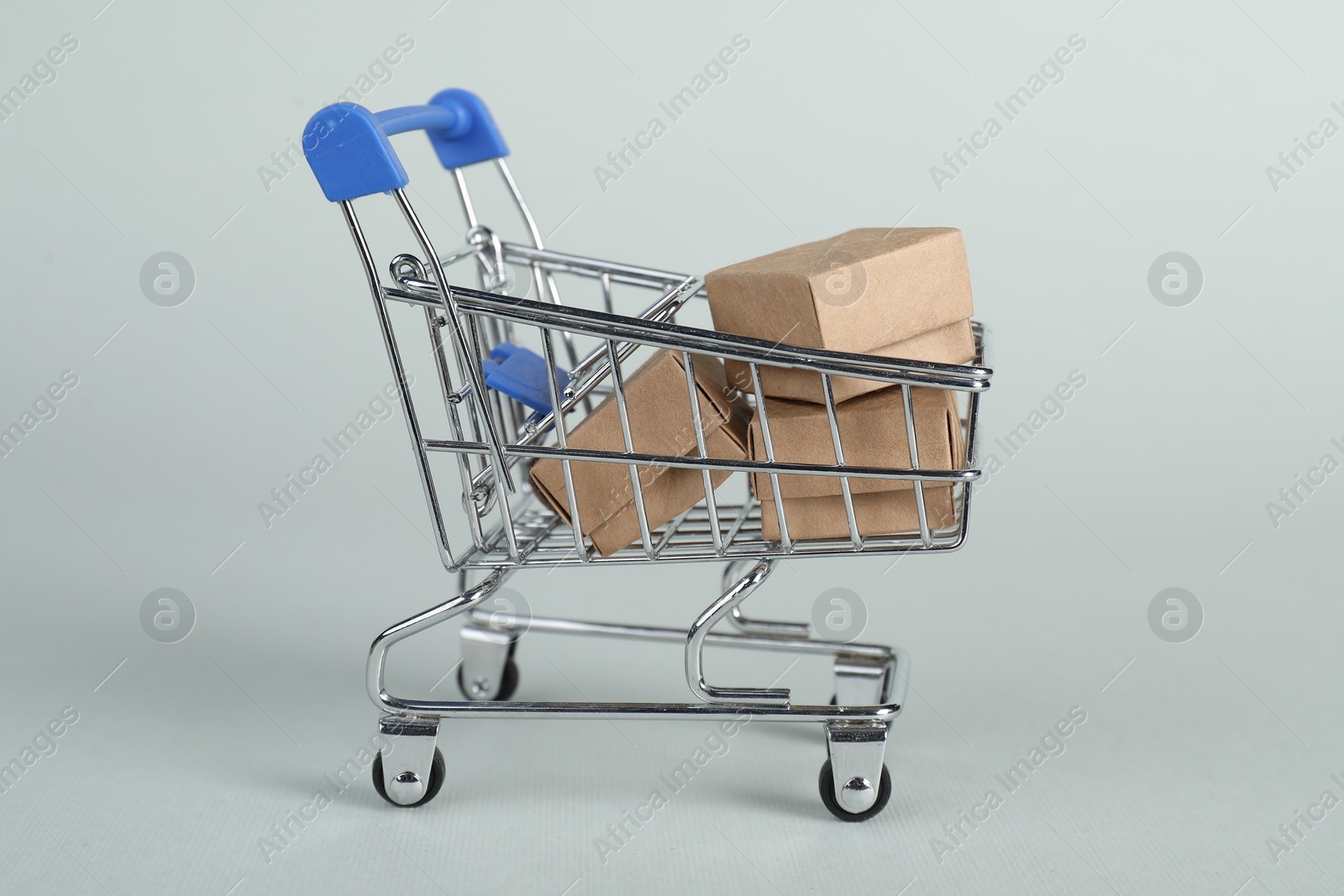 Photo of Small metal shopping cart with cardboard boxes on light background