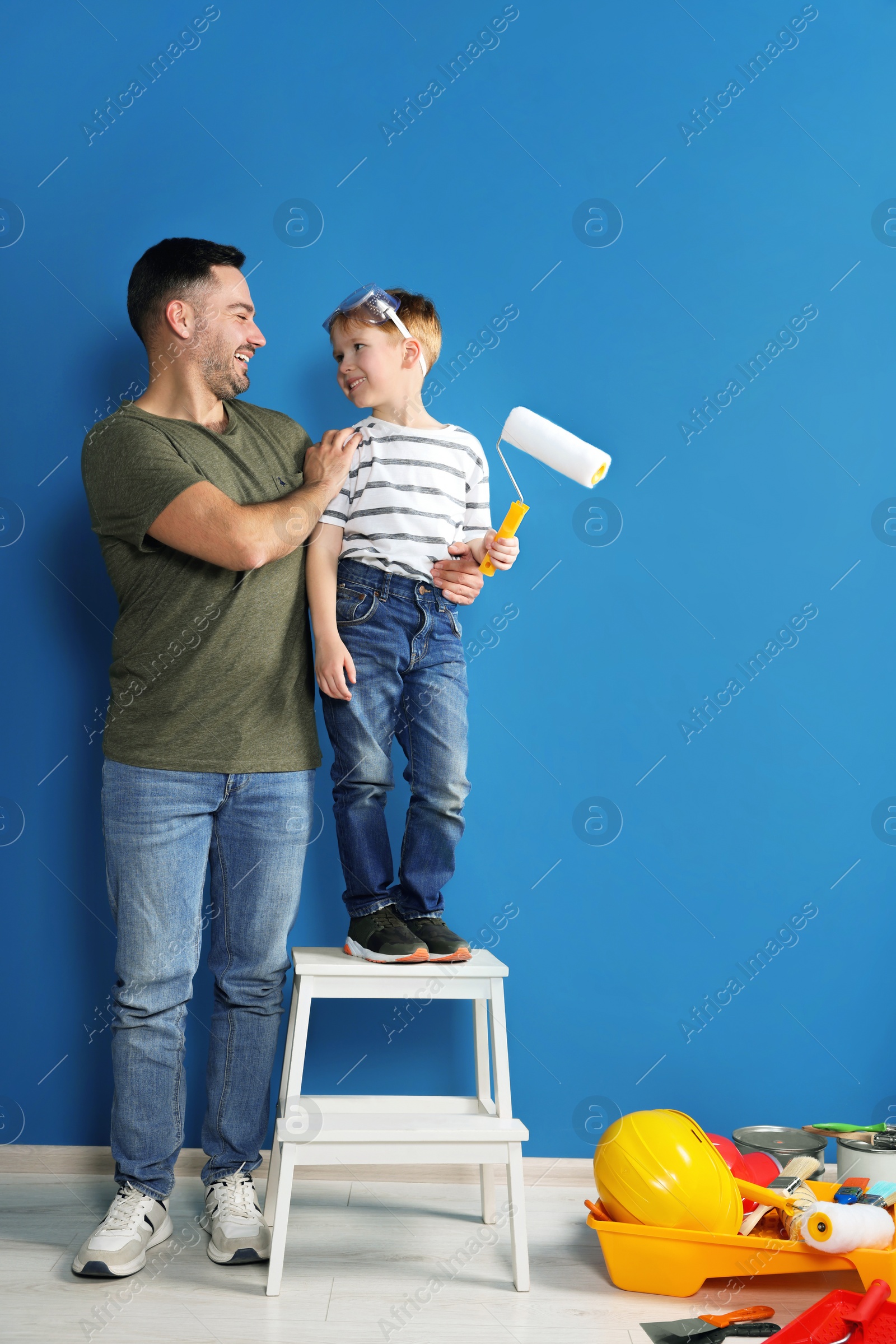 Photo of Father and son with roller near blue wall. Repair work