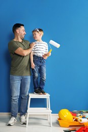 Photo of Father and son with roller near blue wall. Repair work