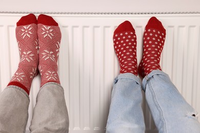 People warming feet near heating radiator, closeup