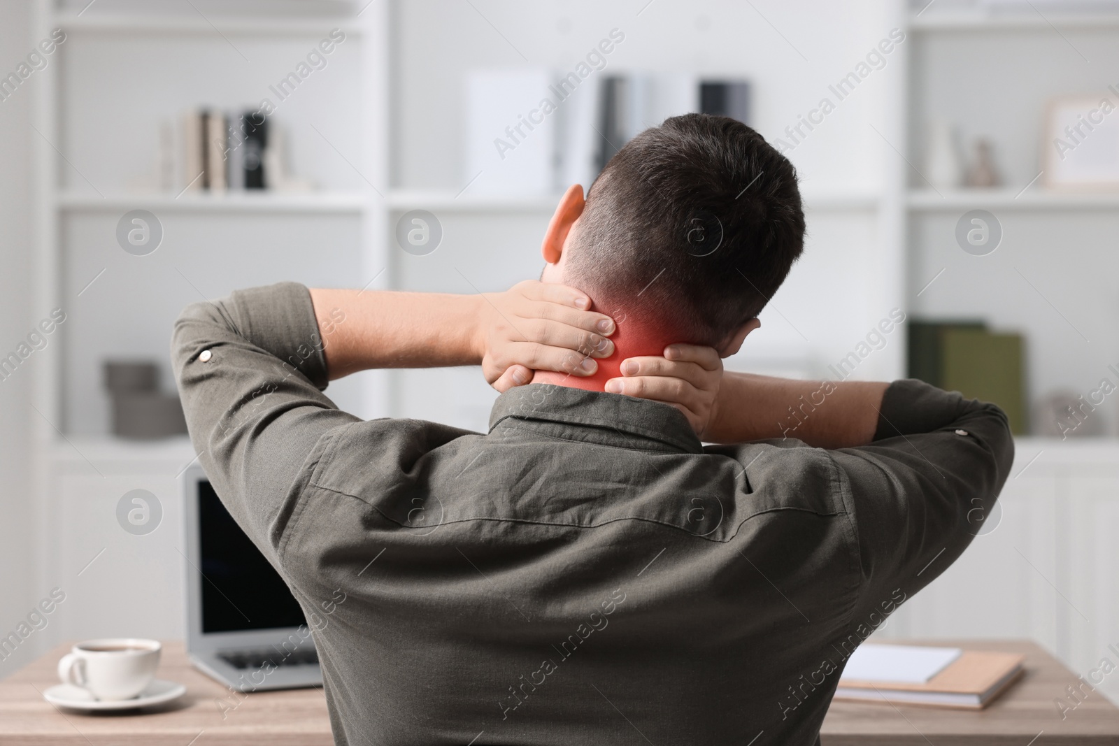 Image of Man suffering from neck pain at table, back view