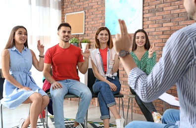 Photo of Group of young people learning sign language with teacher indoors