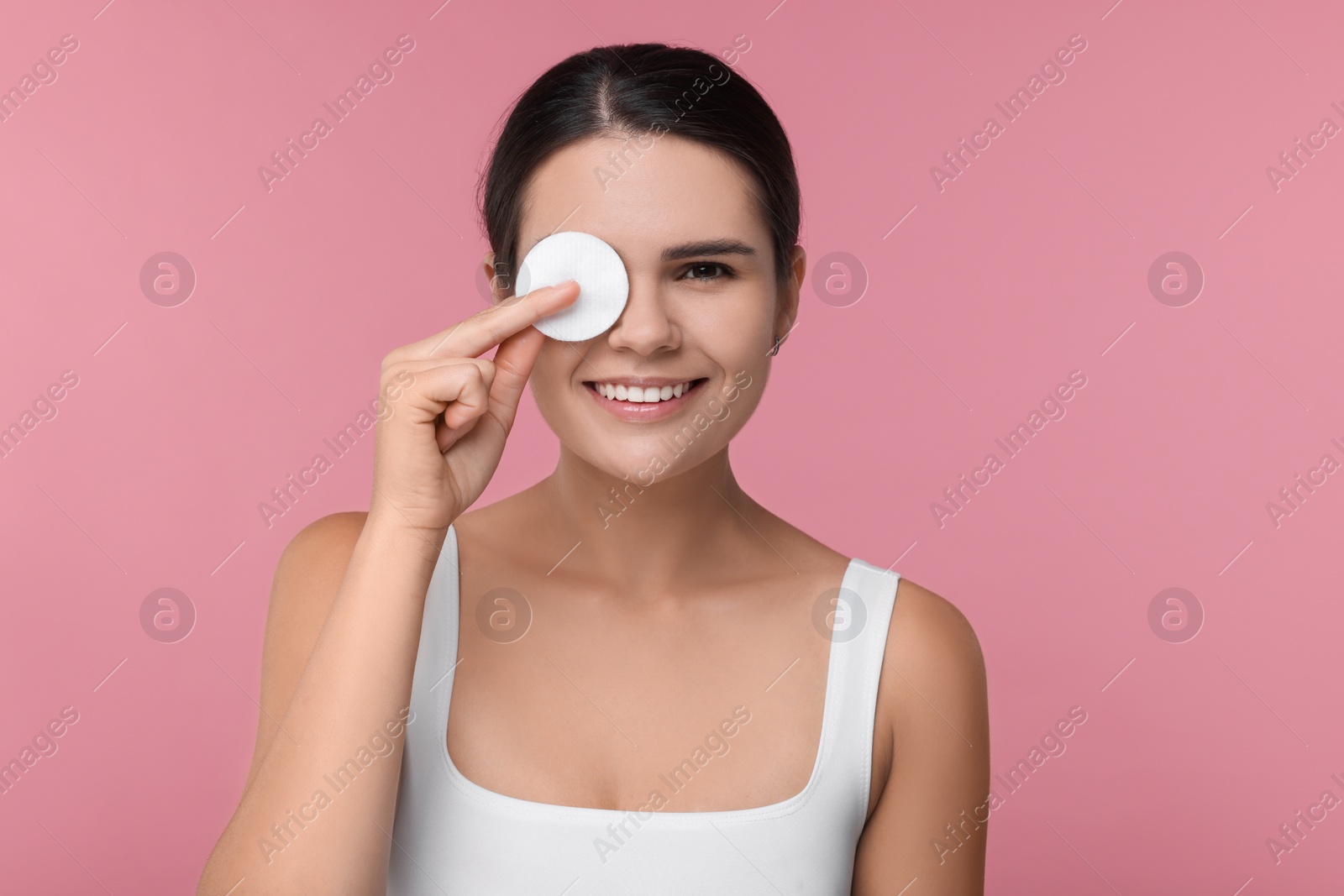 Photo of Young woman cleaning her face with cotton pad on pink background