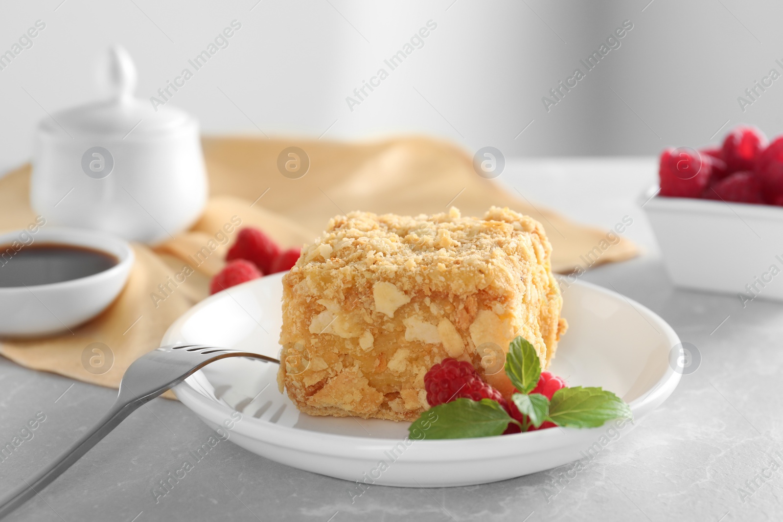 Photo of Piece of delicious Napoleon cake, raspberries and fork on beige table