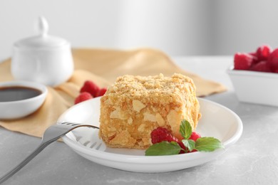 Photo of Piece of delicious Napoleon cake, raspberries and fork on beige table