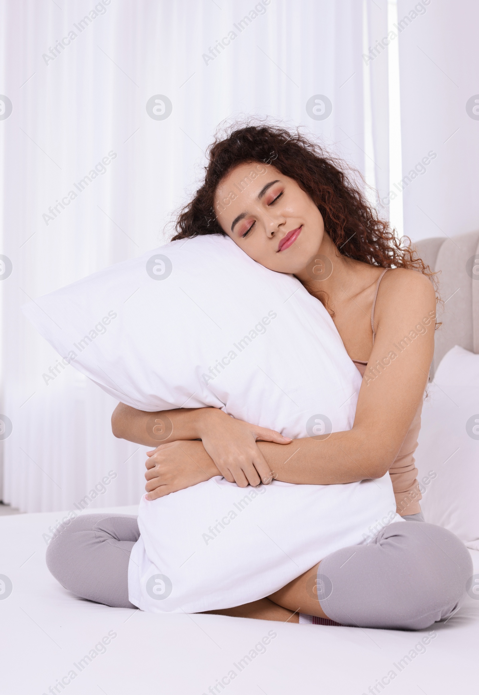 Photo of Happy African American woman hugging soft pillow on bed at home