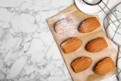 Photo of Delicious madeleine cakes and powdered sugar on white marble table, flat lay. Space for text