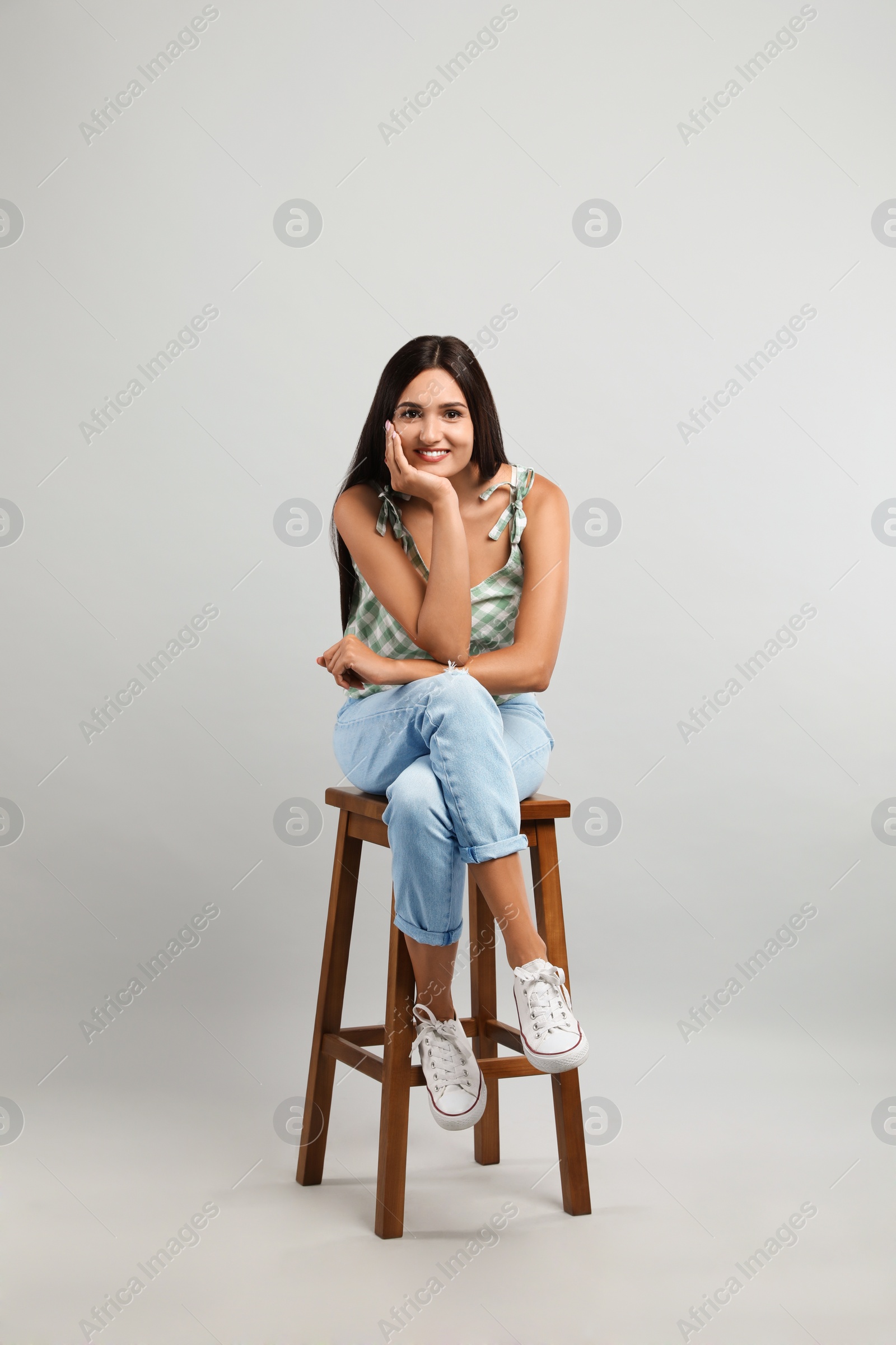 Photo of Beautiful young woman sitting on stool against light grey background