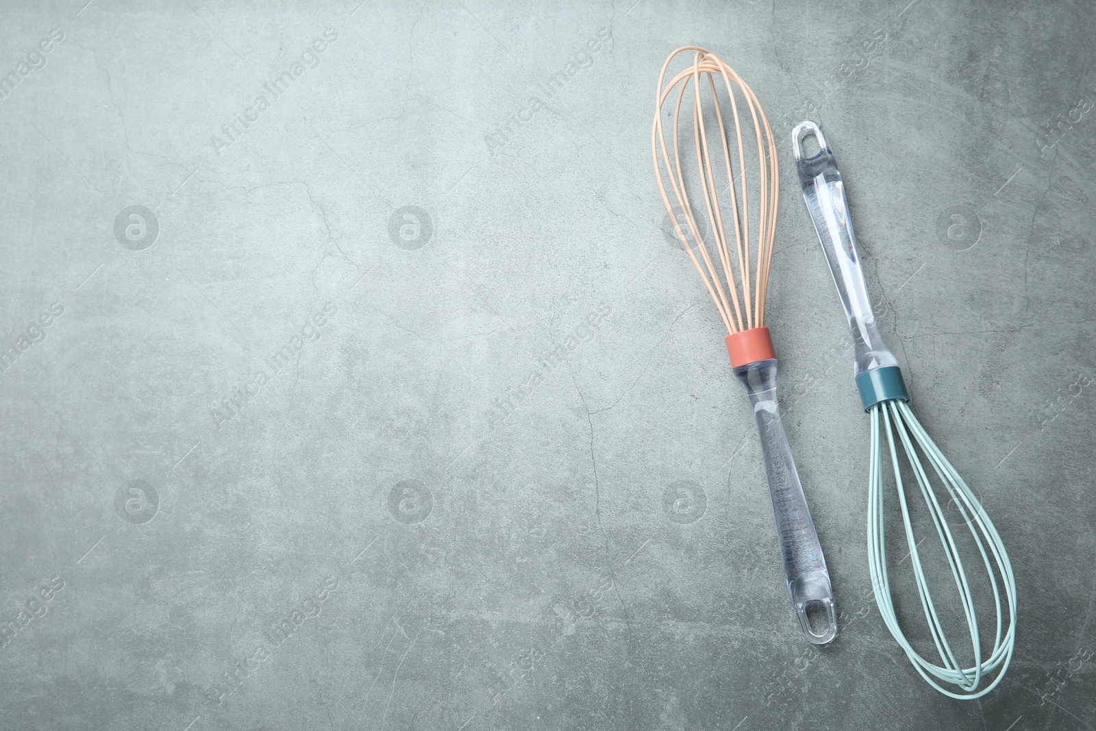 Photo of Two whisks on gray table, top view. Space for text