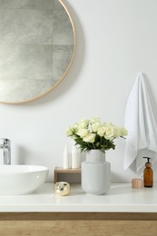 Photo of Vase with beautiful white roses and toiletries near sink in bathroom