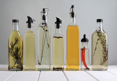 Photo of Bottles of different cooking oils on white wooden table against grey background