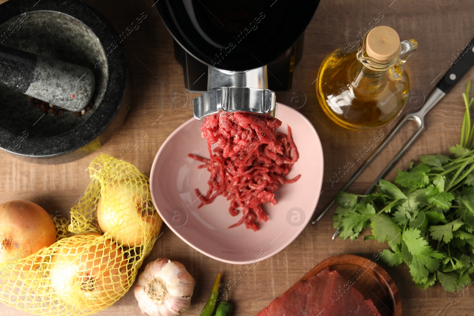 Photo of Mincing beef with electric meat grinder on wooden table, flat lay
