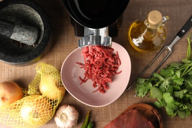 Mincing beef with electric meat grinder on wooden table, flat lay