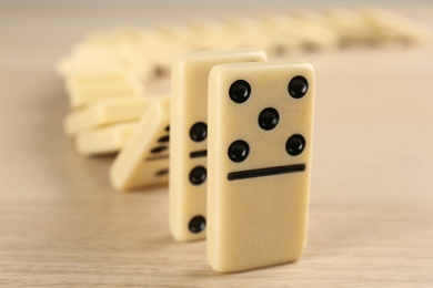 Photo of White domino tiles falling on wooden table, closeup