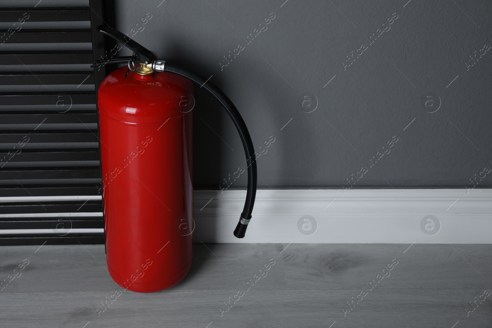 Photo of Fire extinguisher near grey wall indoors. Space for text