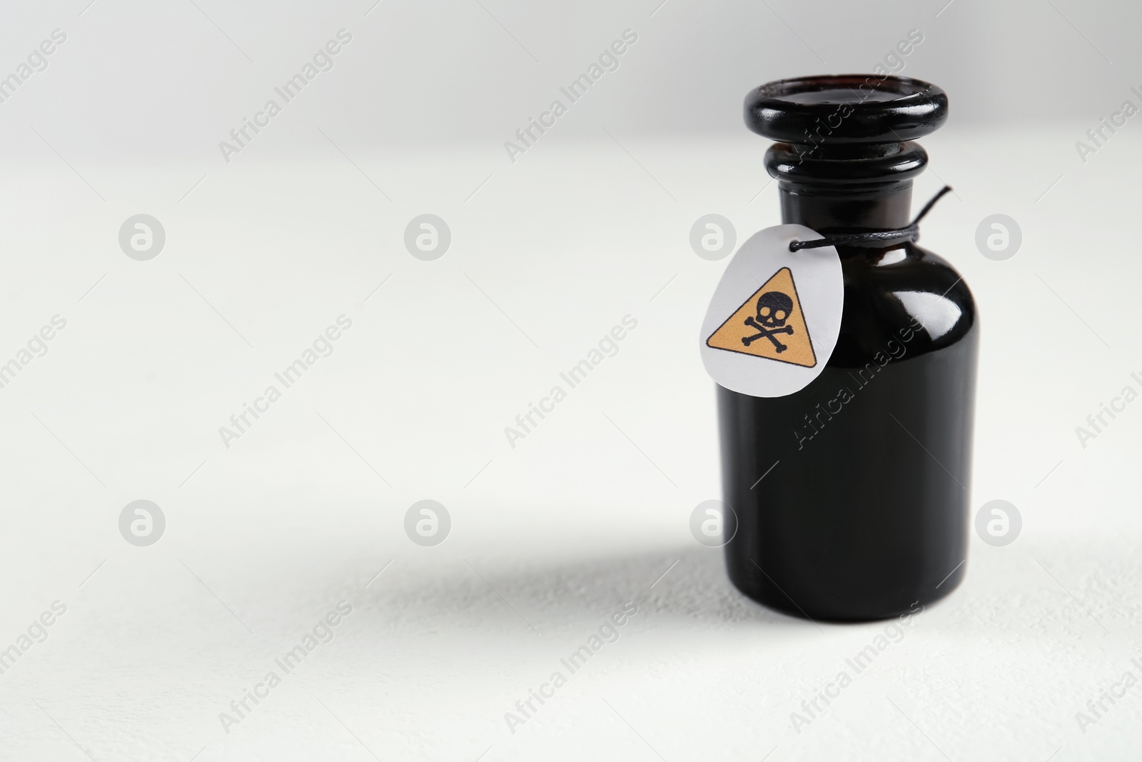 Photo of Glass bottle of poison with warning sign on light background. Space for text