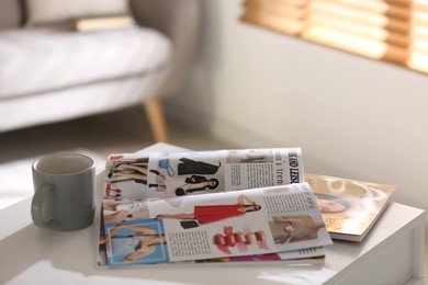 Photo of Fashion magazines and cup of hot drink on white table indoors