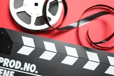 Photo of Clapboard and reel with foil on red background, flat lay. Video production equipment